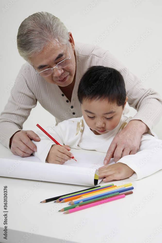 Boy drawing with coloured pencil, senior man watching Boy drawing with coloured pencil, senior man watching