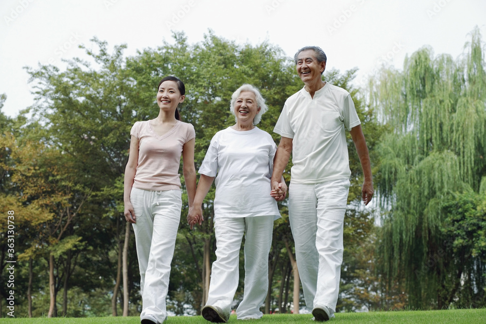 Woman together with senior couple holding hands while walking in the park Woman together with senior couple holding hands while walking in the park