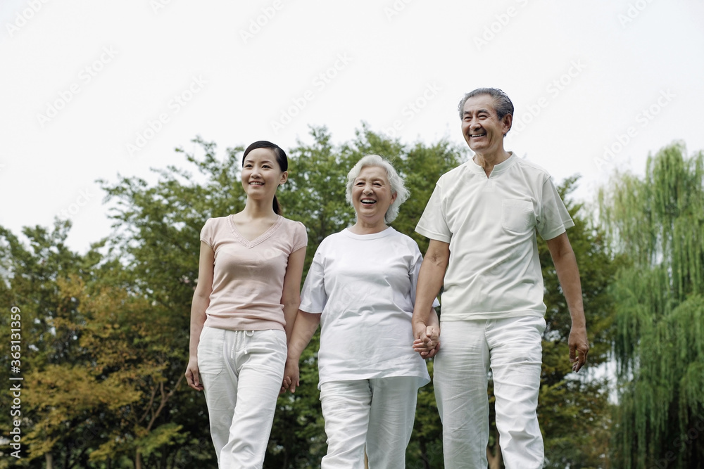 Woman together with senior couple holding hands while walking in the park Woman together with senior couple holding hands while walking in the park