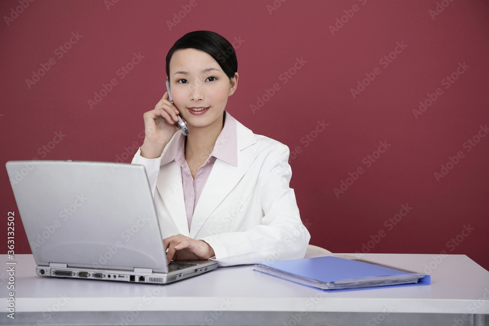 Businesswoman talking on the phone while using laptop Businesswoman talking on the phone while using laptop