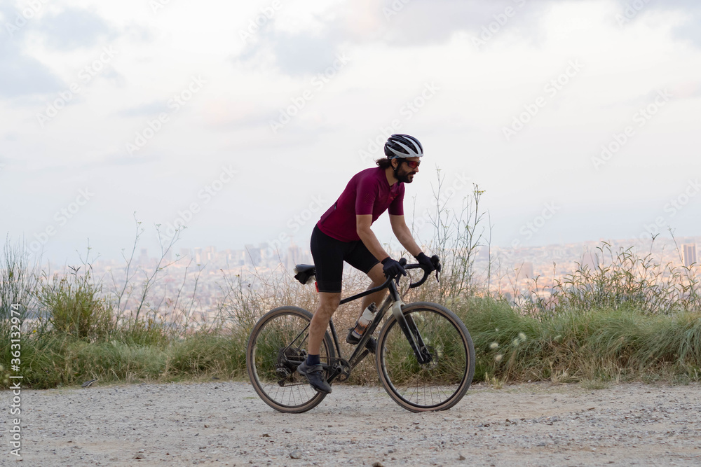 Cyclist man pedaling standing with his gravel bike with the city of Barcelona on the horizon