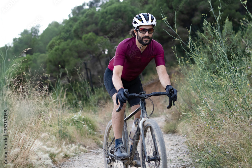 Cyclist man with gravel bike descending a path through the vegetation