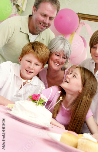 A girl sitting in front of her birthday cake with her parents and siblings surrounding her