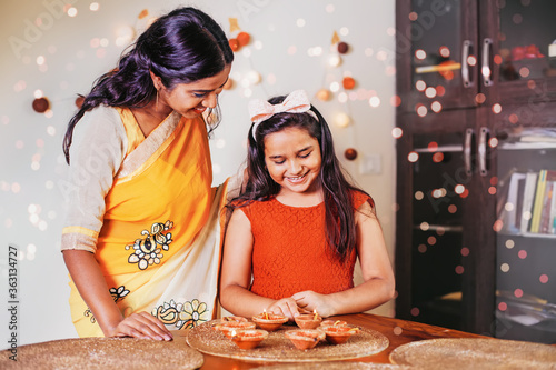 Cute little Indian girl lighting diyas for Diwali together with her mother at home photo