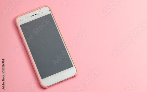 Broken phone with crack on the display glass on pink background. Copy space for text.