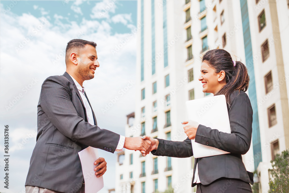 Indian business people, man and woman, shaking hands against the corporate building Indian business people, man and woman, shaking hands against the corporate building