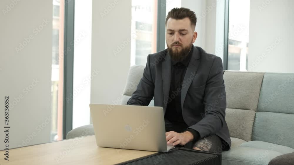 Young beard businessman work at the computer, sitting on sofa in a business building. Young beard businessman work at the computer, sitting on sofa in a business building.