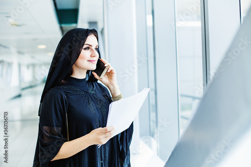 Photography Beautiful arab woman wearing black abaya talking over phone and holding a docume