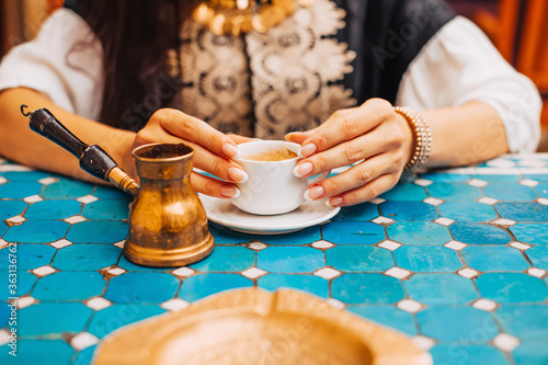 Closeup photo of woman holding a cup of turkish coffee in a cafe with turquoise tiles table photo