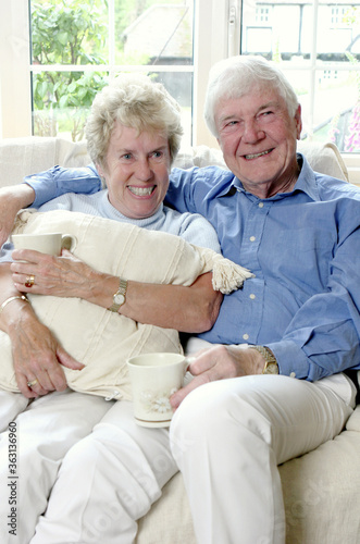 An old man sitting on the couch with his arm around his wife