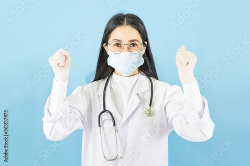 Smart young asian woman doctor in lab coat with Medical face mask,white latex medical gloves and stethoscope against blue background,health care concept