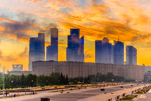 Dawn over Victory Park on Poklonnaya Hill in Moscow in the summer. Fiery orange sky with foggy clouds and sunrise over the silhouettes of Moscow City skyscrapers.