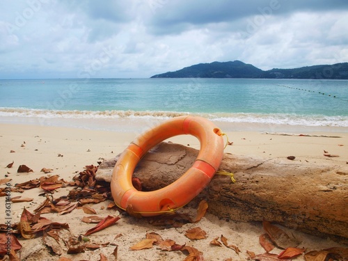 Lifebuoy on the beach, dry leaves on the sand, island, water, sea. Lifeguard equipment. Panoramic view of empty beach in the autumn leaf fall season. Cloudy sky before rain. Close-up, macro, isolated 