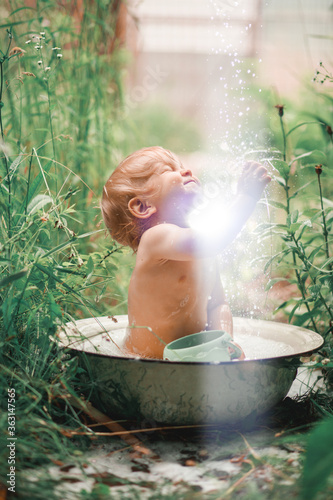 Sunny summer day.A charming little boy is bathing in a baby bath on a green lawn.He splashed and laughed.
