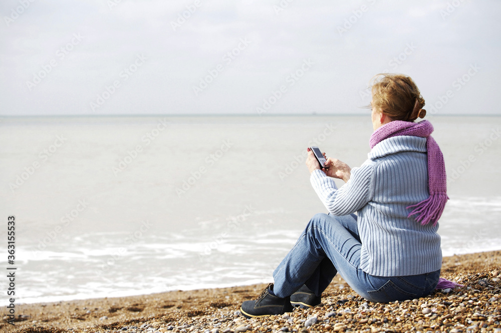 A woman sitting on the beach while using her mobile