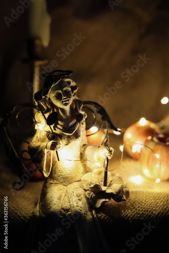 sculpture of a sitting angel against a burning candle and yellow garlands in the dark