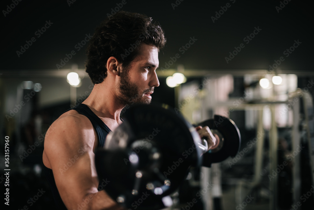 Handsome bearded young man with muscular wiry body wearing sportswear working out with barbell during sport workout training in modern dark gym. Concept of healthy lifestyle. Handsome bearded young man with muscular wiry body wearing sportswear working out with barbell during sport workout training in modern dark gym. Concept of healthy lifestyle.