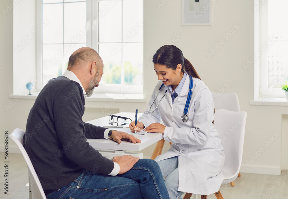 Obraz premium Female doctor writing medication order for senior patient in clinic. Elderly man on visit to his healthcare provider