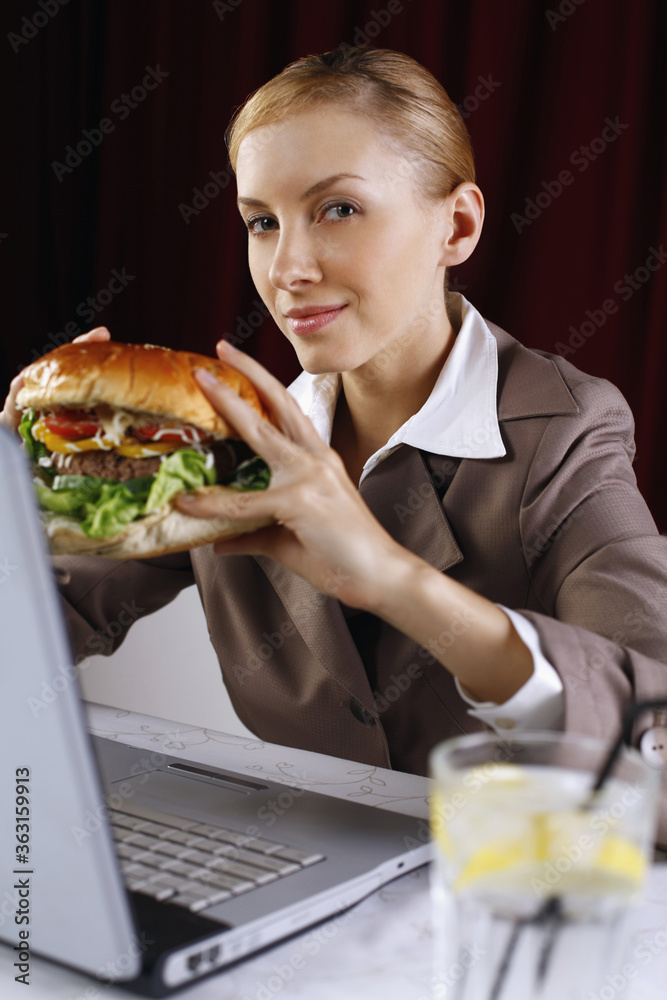 Businesswoman holding burger while using laptop at her table