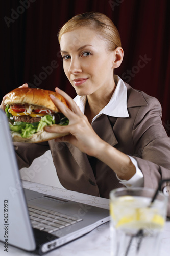 Businesswoman holding burger while using laptop at her table © ImageHit