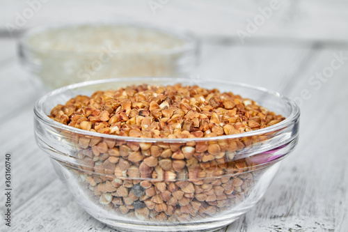 Raw white rice and buckwheat groats in a transparent glass plate on wooden background. Closeup