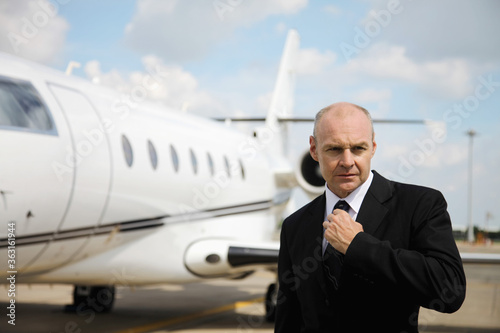 Businessman adjusting his tie on runway with private jet in the background