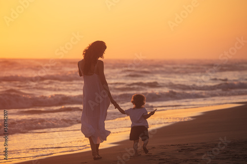 A mom with her child walk on the beach of a beautiful shore at the sunset light