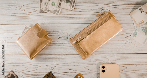 Two gold wallets, plastic cards, dollars, rubles, an expensive smartphone with two cameras on a wooden board background.