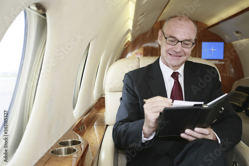 Businessman writing in organizer on private jet © ImageHit