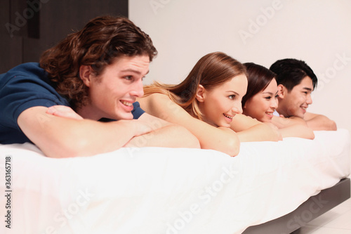 Men and women lying on bed covered by comforter