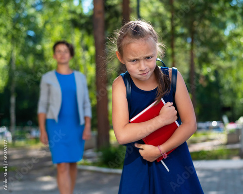 Unhappy girl with a book does not want to go to school. Mother sends daughter to first grade. The first day in elementary school.