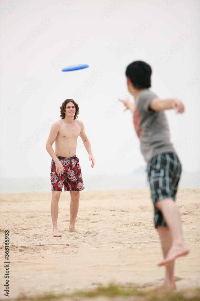 Men playing with flying disc on the beach Men playing with flying disc on the beach