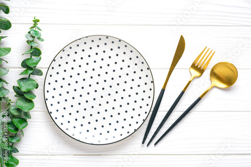 empty white round plate with black peas, fork, knife, spoon, sprig of eucalyptus on wooden table Top view Flat lay Dishes for breakfast, lunch or dinner Mock up