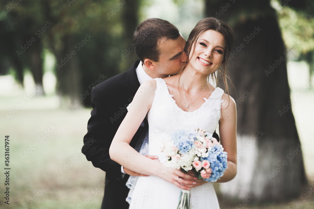 Fototapeta premium Stylish couple of happy newlyweds walking in the park on their wedding day with bouquet