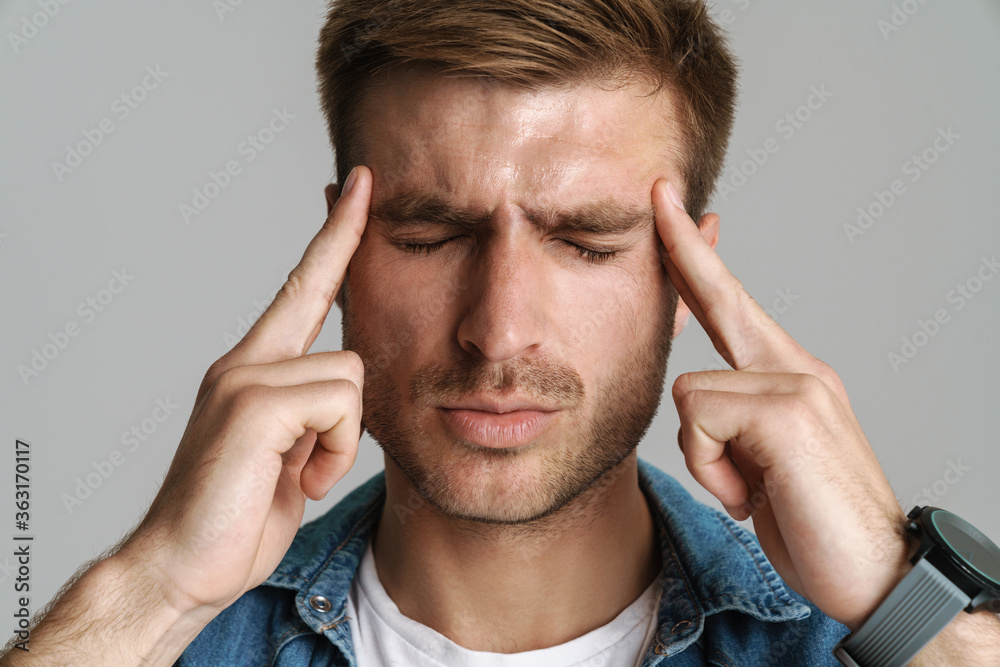 Portrait of unhappy young man with headache rubbing his temples Portrait of unhappy young man with headache rubbing his temples