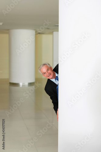 Businessman smiling from behind a pillar