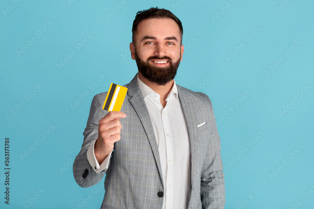 Cheerful company employee holding credit card on blue background Cheerful company employee holding credit card on blue background