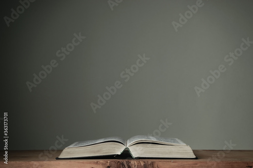 Open Holy Bible on a red wooden table and white wall background. Religion concept.