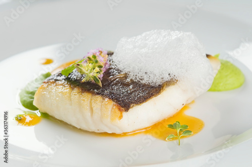 Baked turbot fillet on a white plate. Delicious fish meal with herbs and served with pea puree. Studio shot.