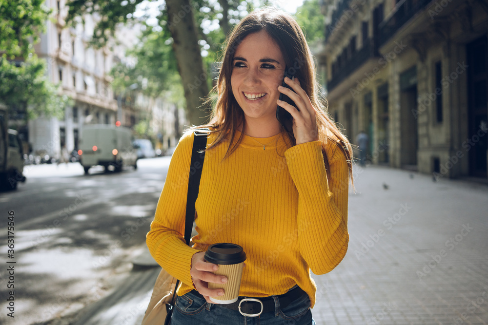 Fototapeta premium Young positive woman smiling while talking on smartphone device, attractive hispanic student girl using her cellphone outdoors