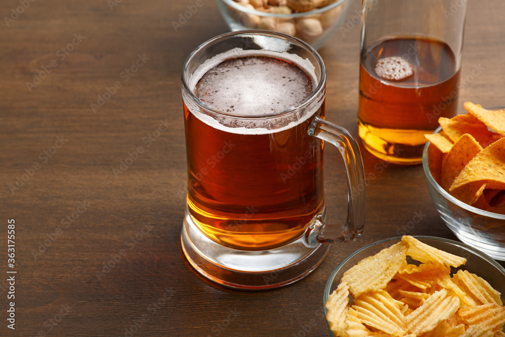 Bright fresh craft beer with foam in mug and bottle. Pistachio, chips and nachos in glass plates Bright fresh craft beer with foam in mug and bottle. Pistachio, chips and nachos in glass plates