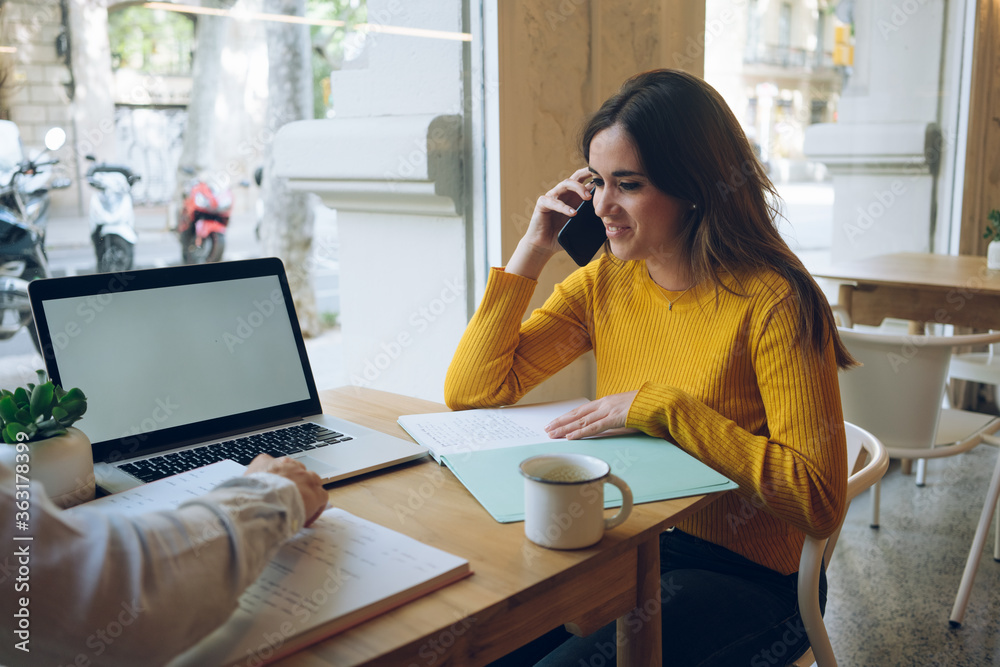 Young girl calling to her colleague  via mobile in coffee shop, attractive modern female student  talking on cell smartphone thinking about her new startup ..