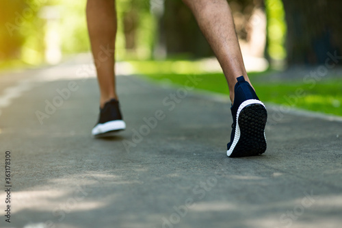 Unrecognizable jogger in sports shoes running at park in morning, close up