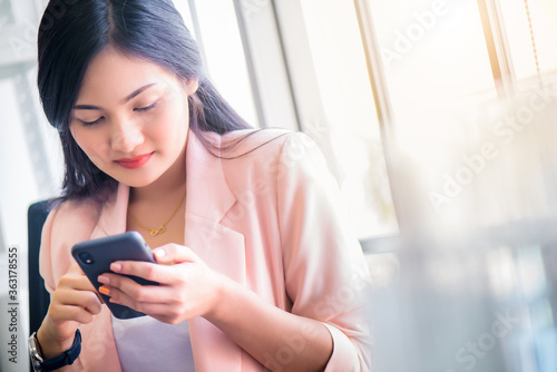Young beautiful smiling Asian woman using smartphone or cellphone to browsing or chatting on social network, internet networking wile relaxing time concept.