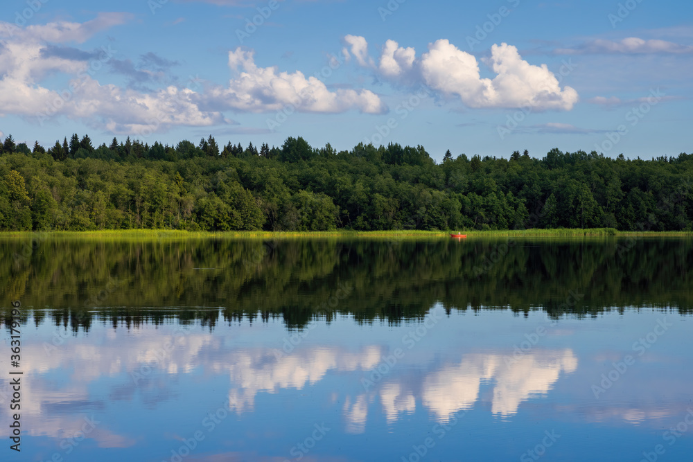 Obraz premium Beautiful summer landscape. View of the lake and forest. Red boat in the distance. Outdoor recreation and fishing on the lake. Clouds are reflected in the water. Travel and vacation in the countryside