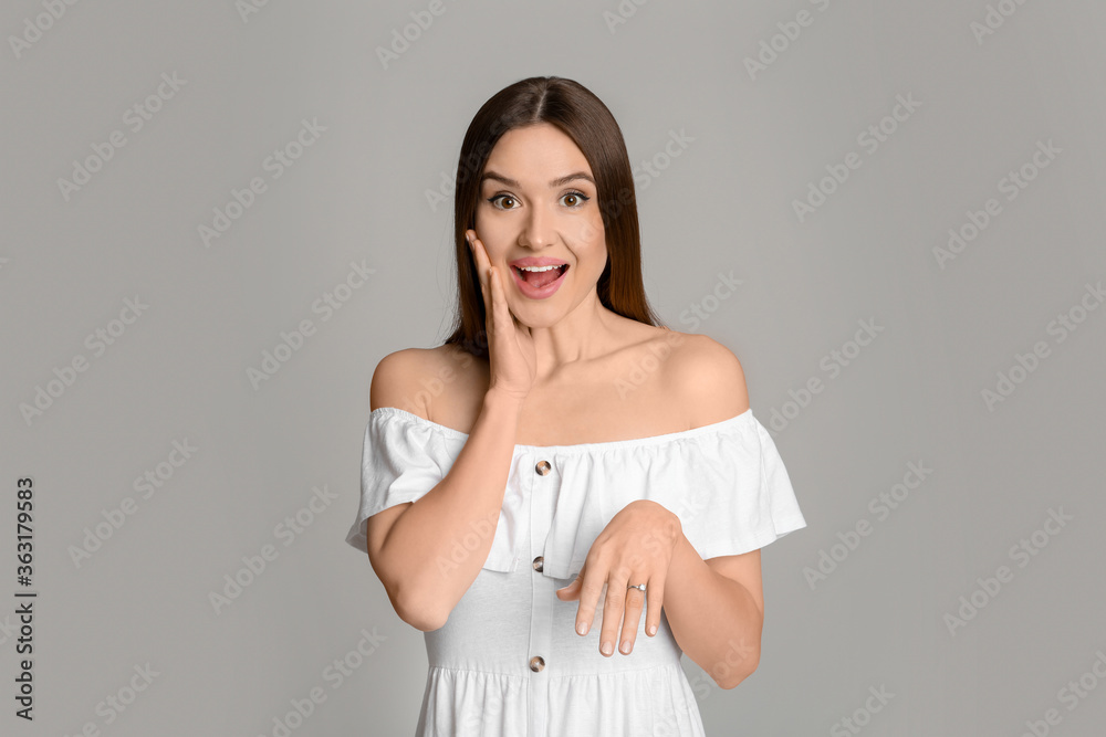 Emotional young woman wearing beautiful engagement ring on grey background Emotional young woman wearing beautiful engagement ring on grey background