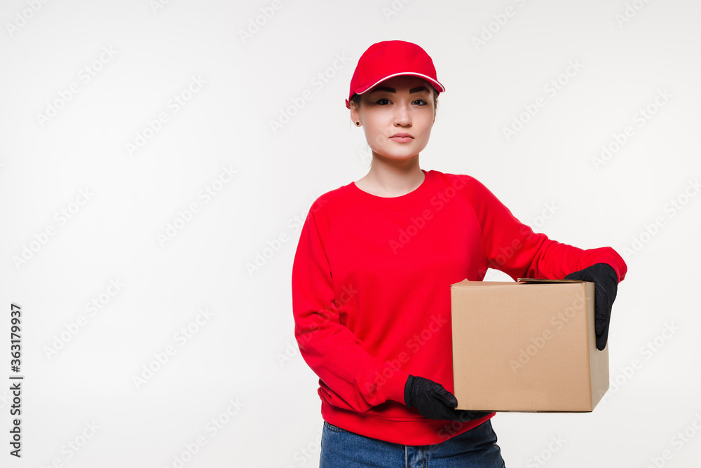 Delivery woman in red uniform isolated on white background. Courier in medical gloves, cap, red t-shirt working as dealer holding cardboard box to deliver. Receiving package. Delivery woman in red uniform isolated on white background. Courier in medical gloves, cap, red t-shirt working as dealer holding cardboard box to deliver. Receiving package.