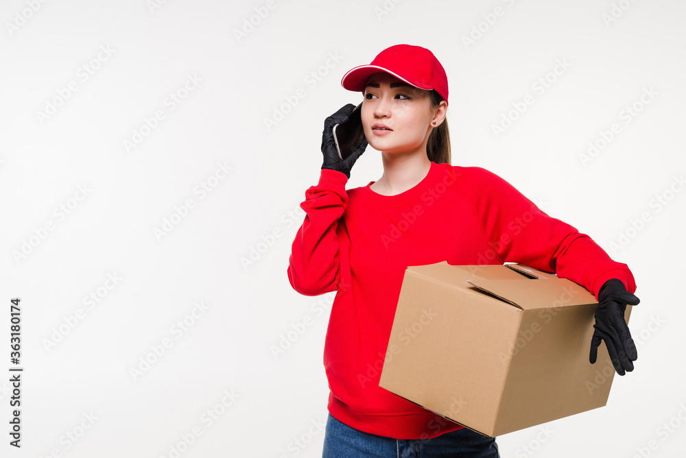 Asian young woman delivery worker standing in white background using mobile smartphone talking with customer checking shipping address