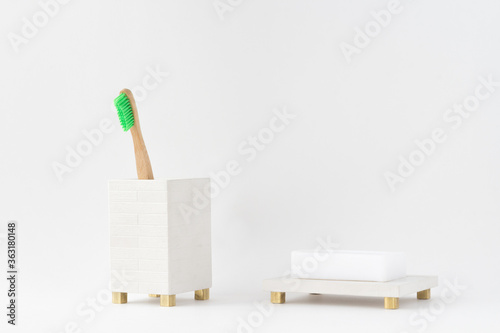 Eco natural wooden bamboo toothbrush in a holder and a soap in a soap dish. Minimal bathroom design, isolated. Natural light.