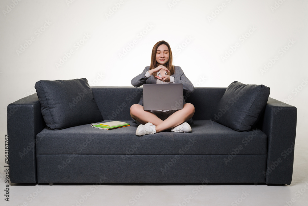 Young asian woman sitting on a sofa using a laptop looking away from the camera isolated on white background Young asian woman sitting on a sofa using a laptop looking away from the camera isolated on white background